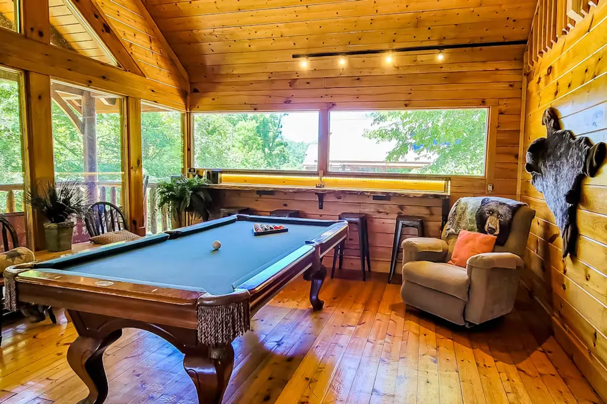 A vibrant game room equipped with a pool table positioned beside large windows, an inviting armchair for relaxing, and plenty of space for friendly competition or lounging. Natural light pours in, creating an energetic and social atmosphere.