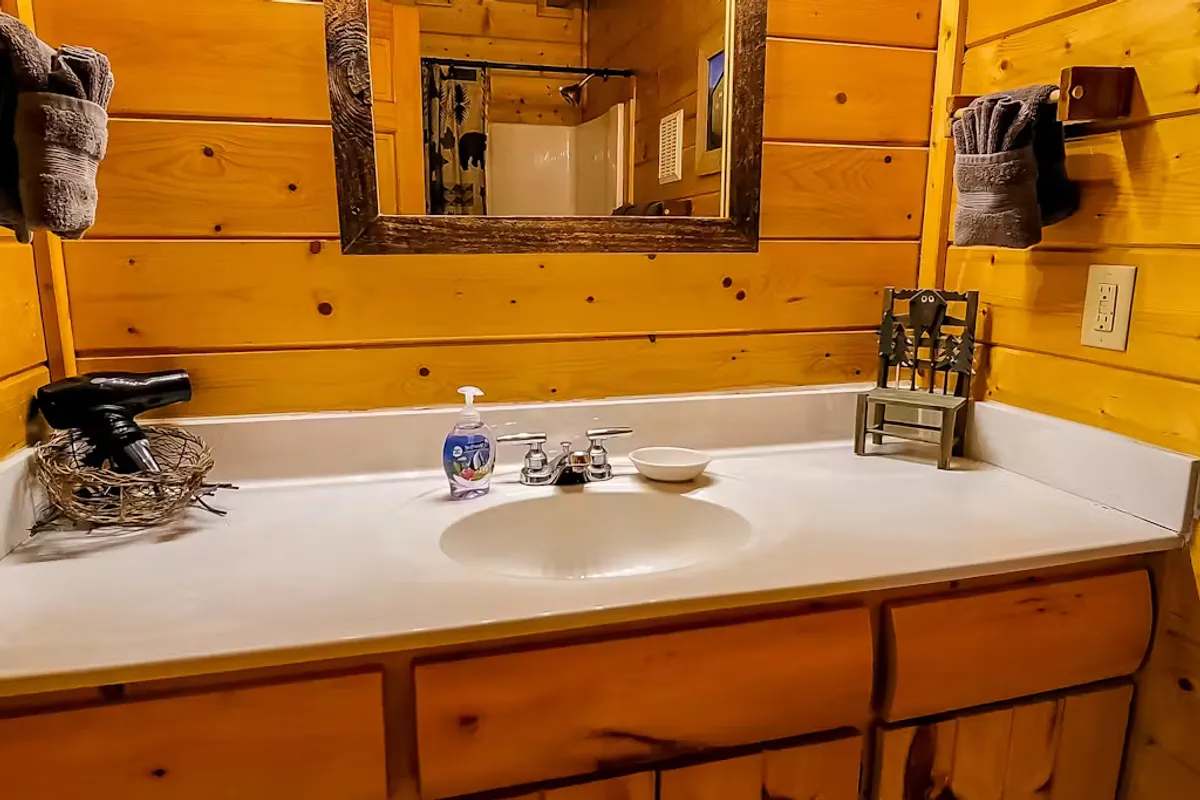 A well-kept bathroom with a sink and mirror, neatly arranged towels, a decorative chair, and warm wooden tones. The ambiance is inviting and functional, perfect for personal care and morning routines.