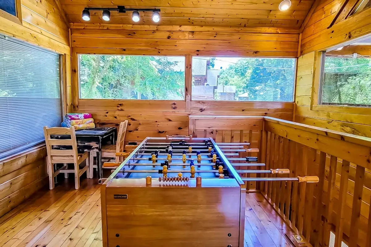Bright game room featuring a foosball table, wooden walls, and large windows that let in natural light and offer glimpses of the surrounding greenery—blending indoor fun with outdoor views.