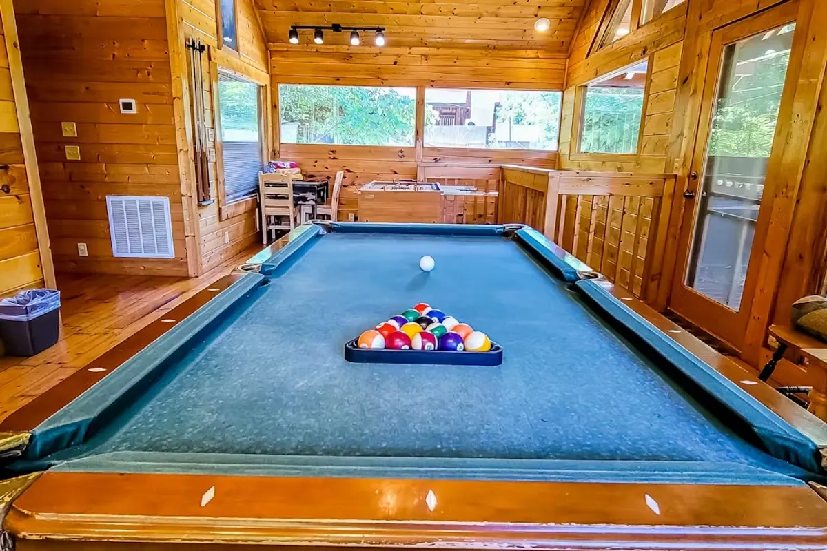 A lively game room interior with a pool table and colorful balls, set against rustic wooden walls. The space is designed for fun, socializing, and friendly competition among friends or family.