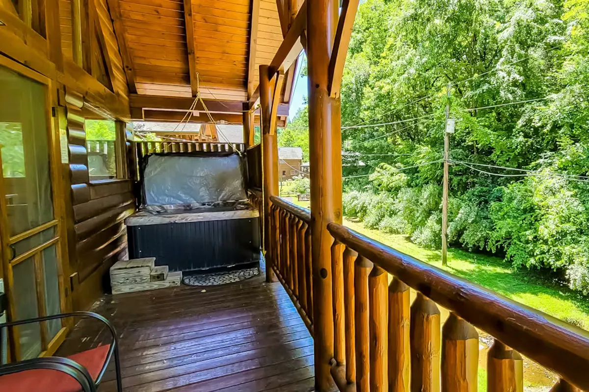 This image showcases a tranquil deck area bordered by a wooden railing, nestled in lush greenery. The private hot tub is the central focus, with inviting outdoor seating and vibrant plant life visible, offering a peaceful, immersive nature experience.