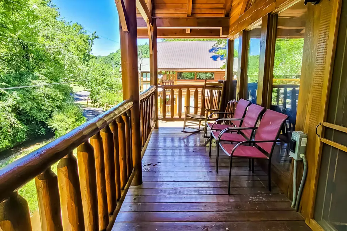The image features an inviting porch with pink chairs, a wooden railing, and a view of vibrant greenery beyond. The setting feels secluded and is ideal for quiet moments, reading, or sharing a drink while enjoying the outdoors.