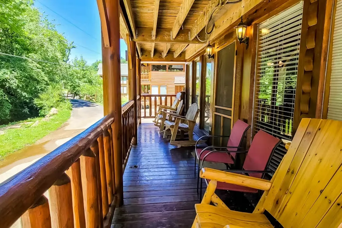 A sun-dappled deck with classic rocking chairs and a wooden railing overlooks a forested area. The morning light filters through the trees, creating a perfect spot for enjoying coffee or watching children play safely nearby.