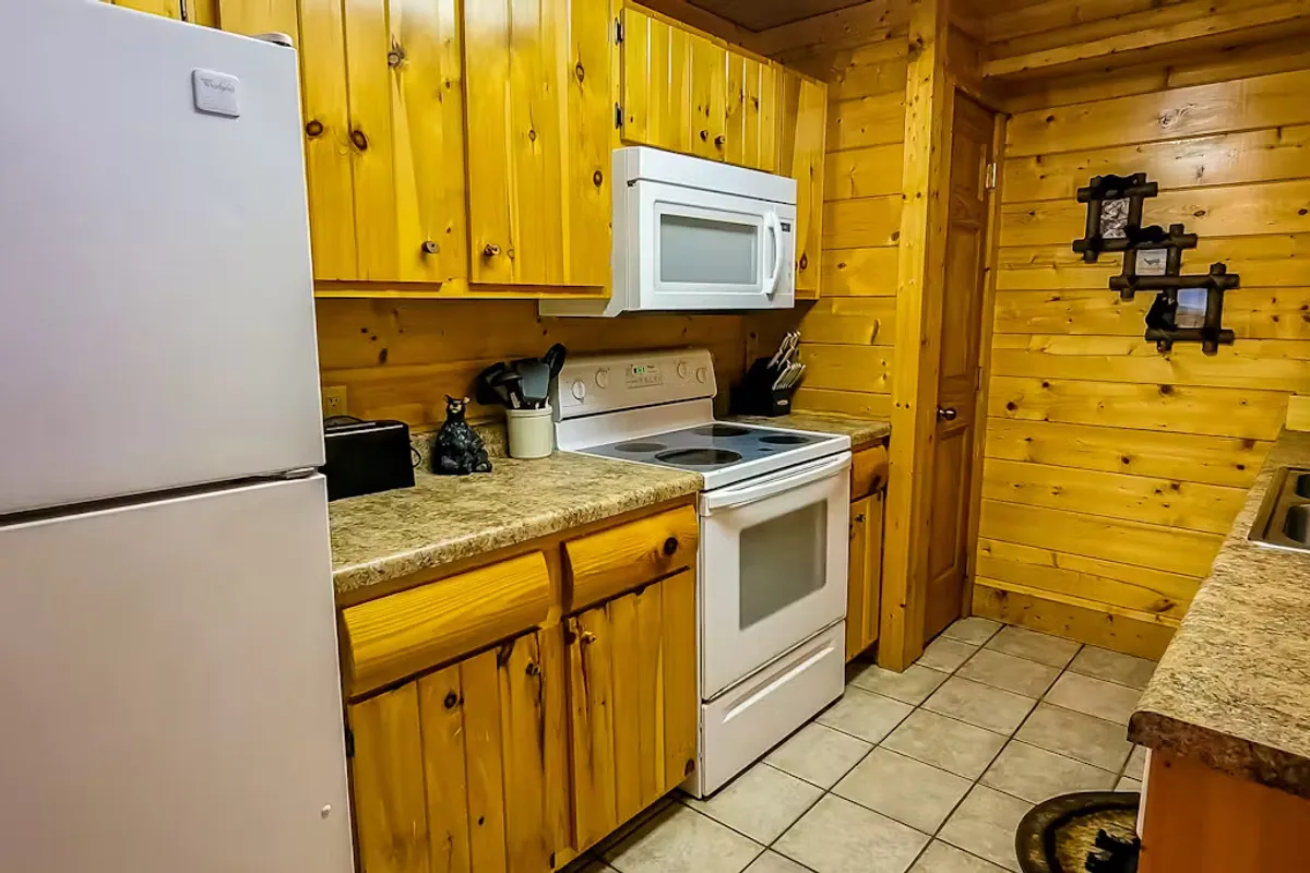 This image offers another perspective of the kitchen area, showcasing wooden cabinetry, white appliances, a spacious granite countertop, and a charming decorative cat figurine. The space looks both functional and homey, ideal for group cooking or casual meals.